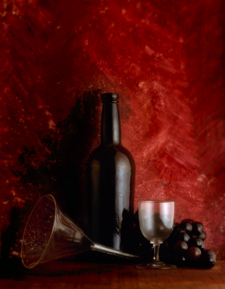 an old port bottle with ged grapes and a glass funnel sit in a terracota ground
